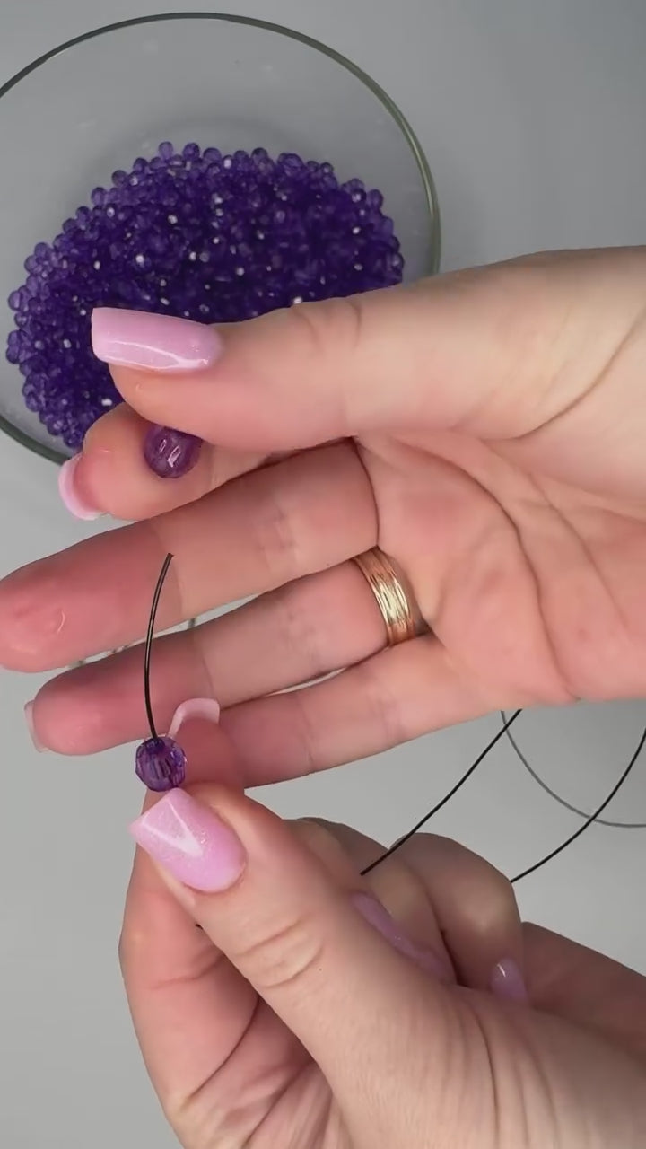 Hands threading violet beads and weaving a beaded panel